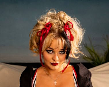 Blonde woman in a vintage outfit with red ribbons and dramatic makeup.